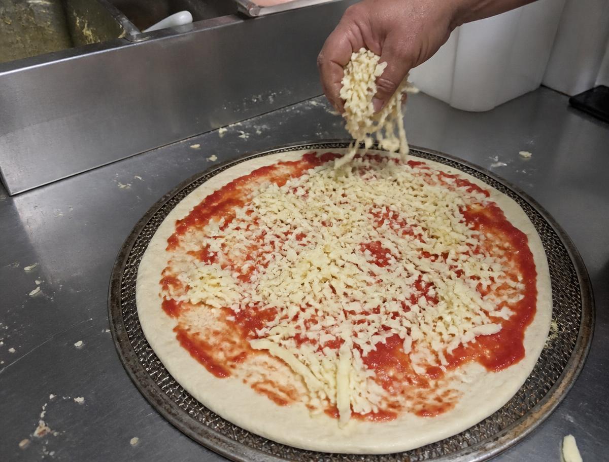Pizza wird in der Küche mit Tomatensugo und Gouda belegt